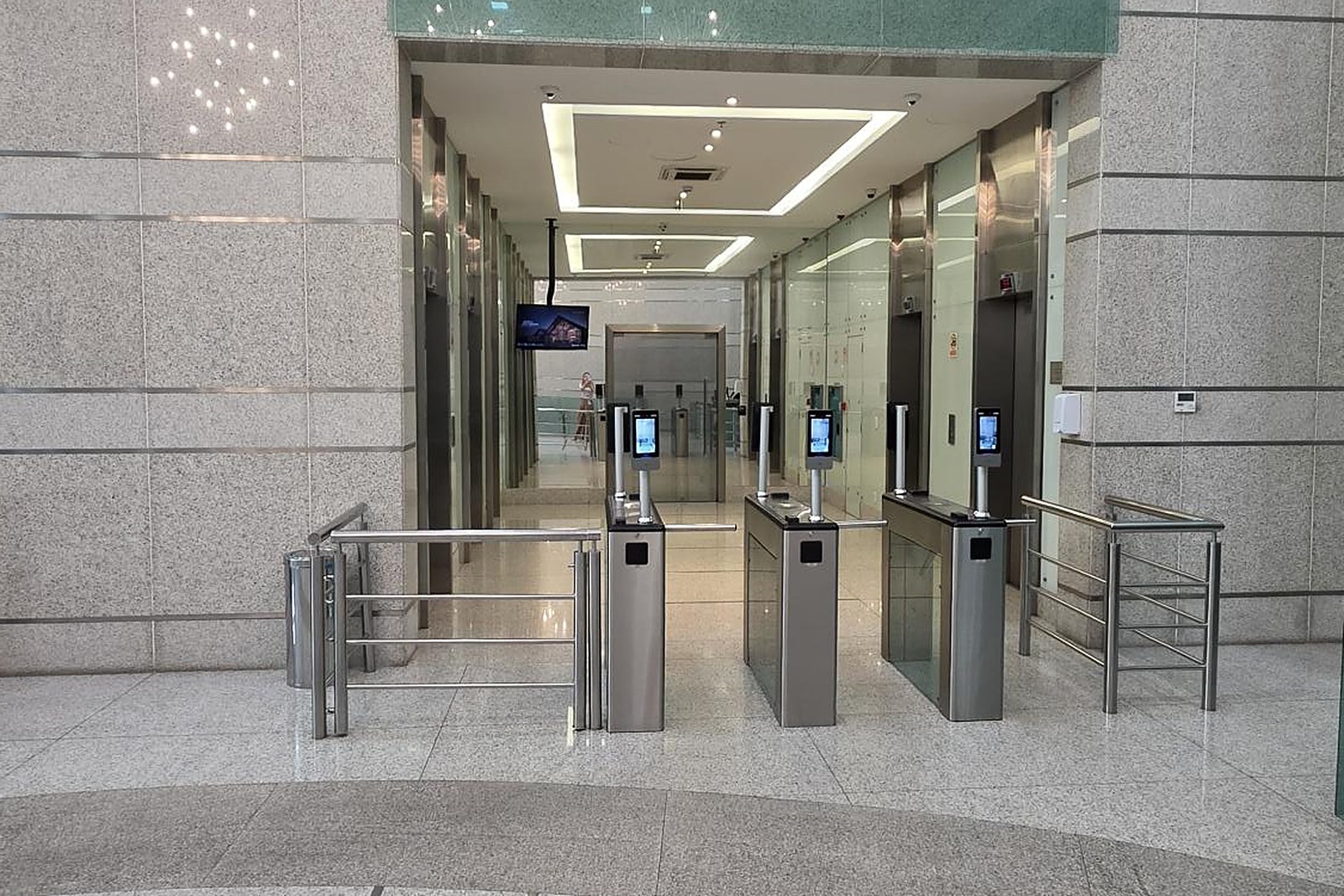 Hall de elevadores do térreo, com catracas de biometria facial e o corredor de acesso aos elevadores.